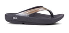 The OOFOS OOlala Luxe Sandal for women is a single black and metallic silver sandal featuring OOfoam technology, a thick sole, textured footbed, and two small white circles on the side.