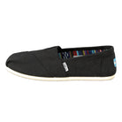 The TOMS Classic Canvas - Men is a black slip-on featuring a white sole, visible side tag, patterned lining, and blue-and-white heel logo patch that highlight its iconic alpargata design.