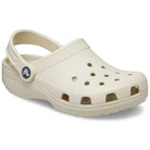 The Crocs Classic Clog - Kids in Bone features a textured sole, ventilation holes on top and sides, and an adjustable heel strap with the Crocs logo.