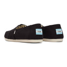 A pair of TOMS Classic Canvas - Men shoes in black recycled cotton canvas with white soles, shown from the back and side. Each slip-on features a small blue and white TOMS logo tag on the heel.