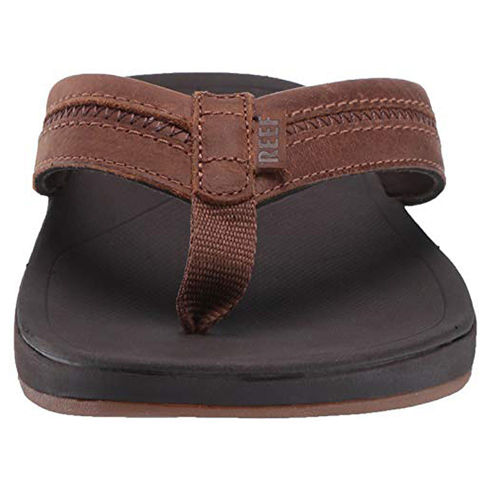 Front view of the Reef Ortho Coast Leather - Men sandal in brown, featuring a leather strap with embossed branding, fabric toe post, orthotic arch support, cushioned footbed, and flat sole.