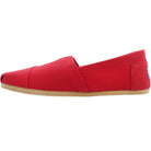 A side view of the TOMS Classic Canvas - Men slip-on shoe in red, featuring a flat light brown sole and a small blue and white TOMS label on the heel.