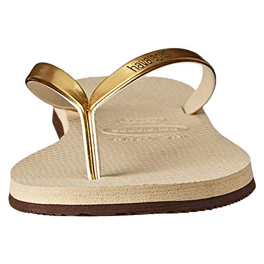 A close-up front view of the Havaianas Slim Metalic - Womens sandal in beige, featuring metallic gold straps with the Havaianas logo embossed, a textured footbed, and a slightly raised sole.
