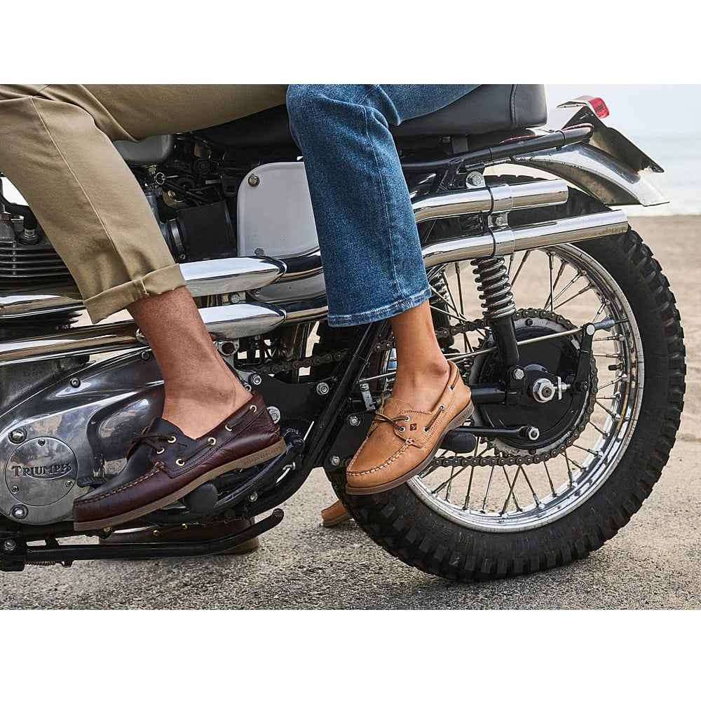 Two people sit on a motorcycle. One wears tan pants with Sperry A/O 2-Eye Leather mens boat shoes, the other blue jeans with light tan boat shoes. Only their legs and feet are visible as the motorcycle rests on pavement.