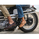 Two people sit on a motorcycle. One wears tan pants with Sperry A/O 2-Eye Leather mens boat shoes, the other blue jeans with light tan boat shoes. Only their legs and feet are visible as the motorcycle rests on pavement.