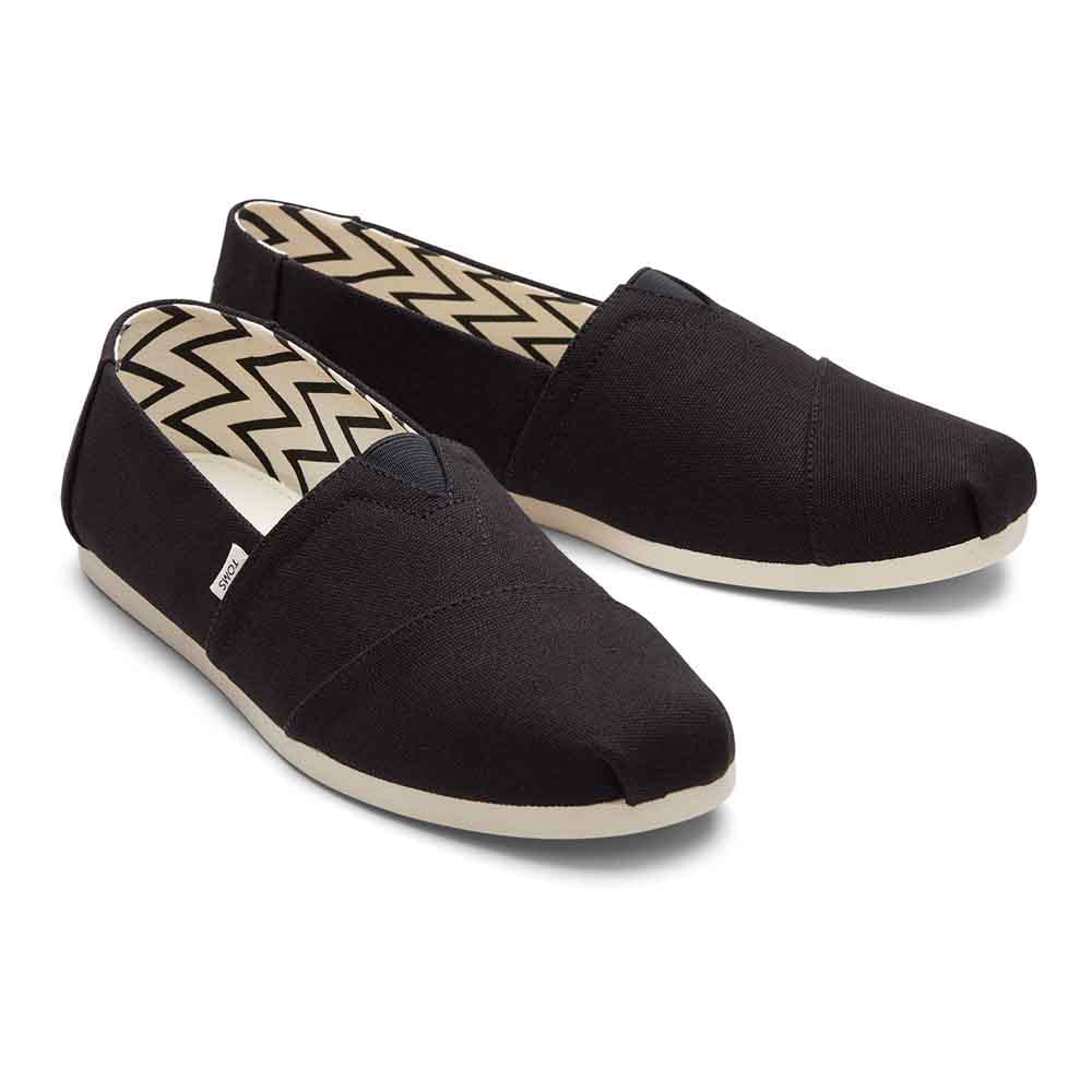 A pair of TOMS Classic Canvas - Men black alpargata slip-on shoes with white rubber soles and chevron-patterned lining, displayed side by side on a white background.