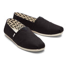 A pair of TOMS Classic Canvas - Men black alpargata slip-on shoes with white rubber soles and chevron-patterned lining, displayed side by side on a white background.