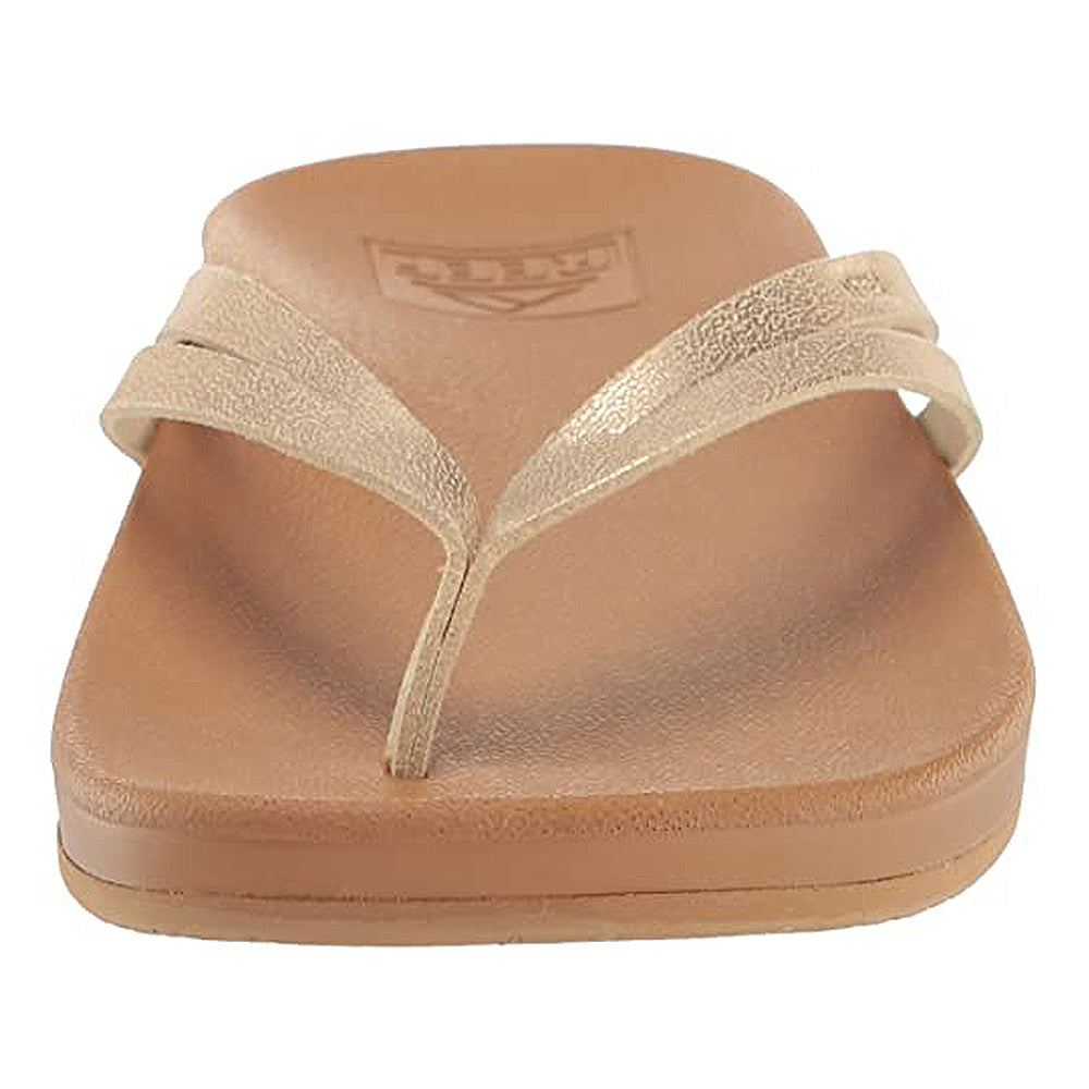 A front view of the Reef Cushion Spring Joy - Womens sandal in tan, featuring a metallic beige thong strap and a flat, textured cushion footbed—ideal for women seeking stylish and comfortable flip flops.