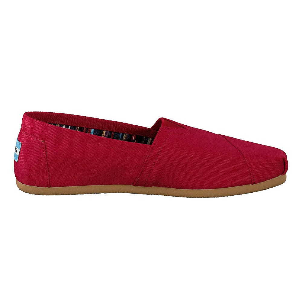 The TOMS Alpargata ESP - Women is a red canvas slip-on with a brown rubber sole, shown from the side. It has a striped inner lining and a blue and white heel label for classic style.