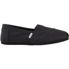 The TOMS Classic Canvas - Men is a black slip-on shoe with a low profile, flat sole, minimalist design, visible stitching, and a small white TOMS label on the side, showcasing the classic style of the brand.
