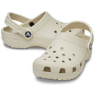 A pair of beige Crocs Classic Clog - Kids shoes with ventilation holes and adjustable heel straps, shown on a white background.