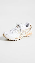 The ASICS Gel-Kayano 14 - Womens features a white athletic design with light beige accents, mesh details, and a textured sole. Loosely laced and angled on a white background, it includes GEL Technology for comfort.