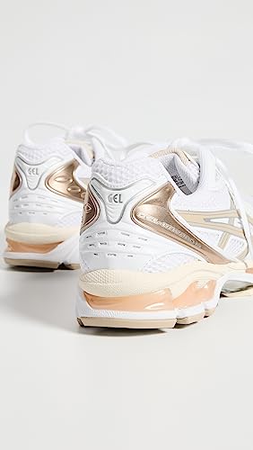 A pair of ASICS Gel-Kayano 14 womens sneakers in white with metallic gold accents, shown from the back and side to highlight the heel details and advanced GEL Technology, displayed on a plain white background.