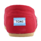 Close-up of the heel of the TOMS Classic Canvas - Men shoe in red, featuring a tan sole and a blue-and-white patch with TOMS in black, highlighting the brands iconic slip-on style.