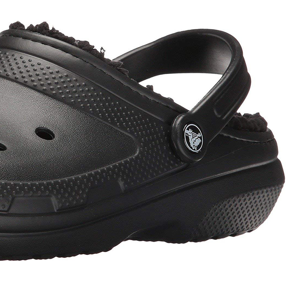 A close-up of the Crocs Classic Lined Clog - Unisex in black, featuring a fuzzy lining, back strap, textured sole, and side ventilation holes—versatile fuzzy clogs for both men and women.