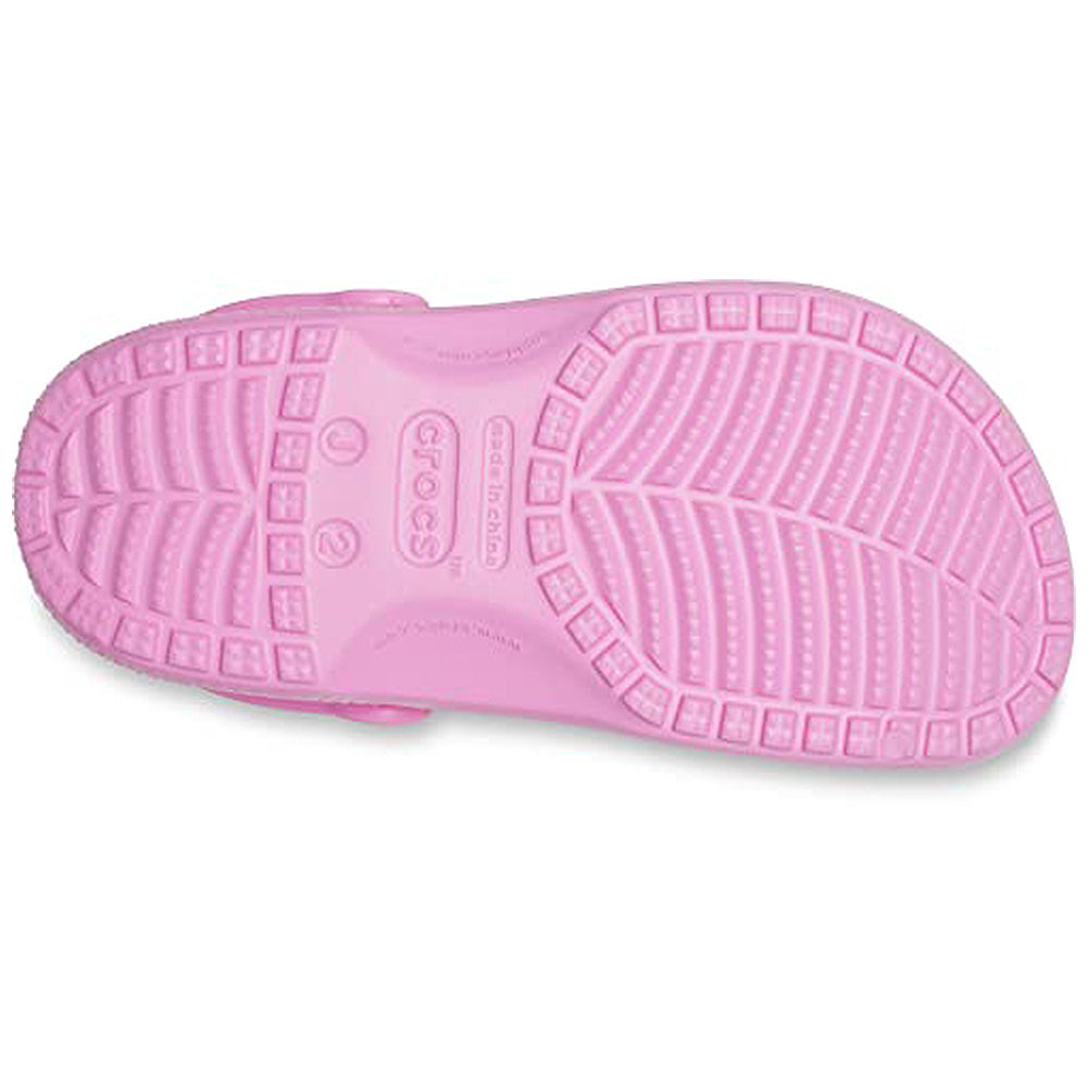 The image shows the sole of the Crocs Classic Clog - Kids in pink, featuring a textured tread for traction. The Crocs brand logo and size markings appear at the center of the sole.
