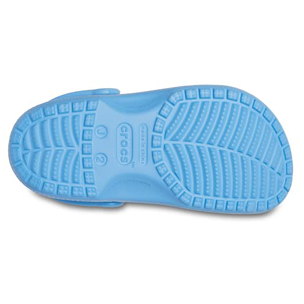 The image displays the sole of a light blue Crocs Classic Clog - Kids, featuring a textured tread with square grips and a leaf pattern in the center. The Crocs logo and shoe sizes are visible on the bottom.