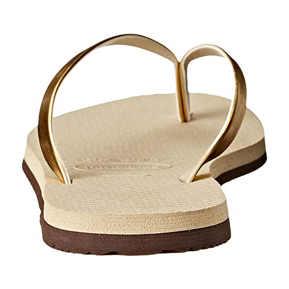 A close-up of the Havaianas Slim Metalic - Womens sandal in beige, featuring gold straps and a textured sole, photographed from heel to toe.