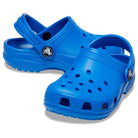 The Crocs Classic Clog - Kids, shown in bright blue with ventilation holes and heel straps, is displayed against a white background.