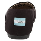 A rear view of the TOMS Alpargata - Womens black canvas slip-on with a light blue and white rectangular TOMS logo label stitched on the heel from the earthwise collection.