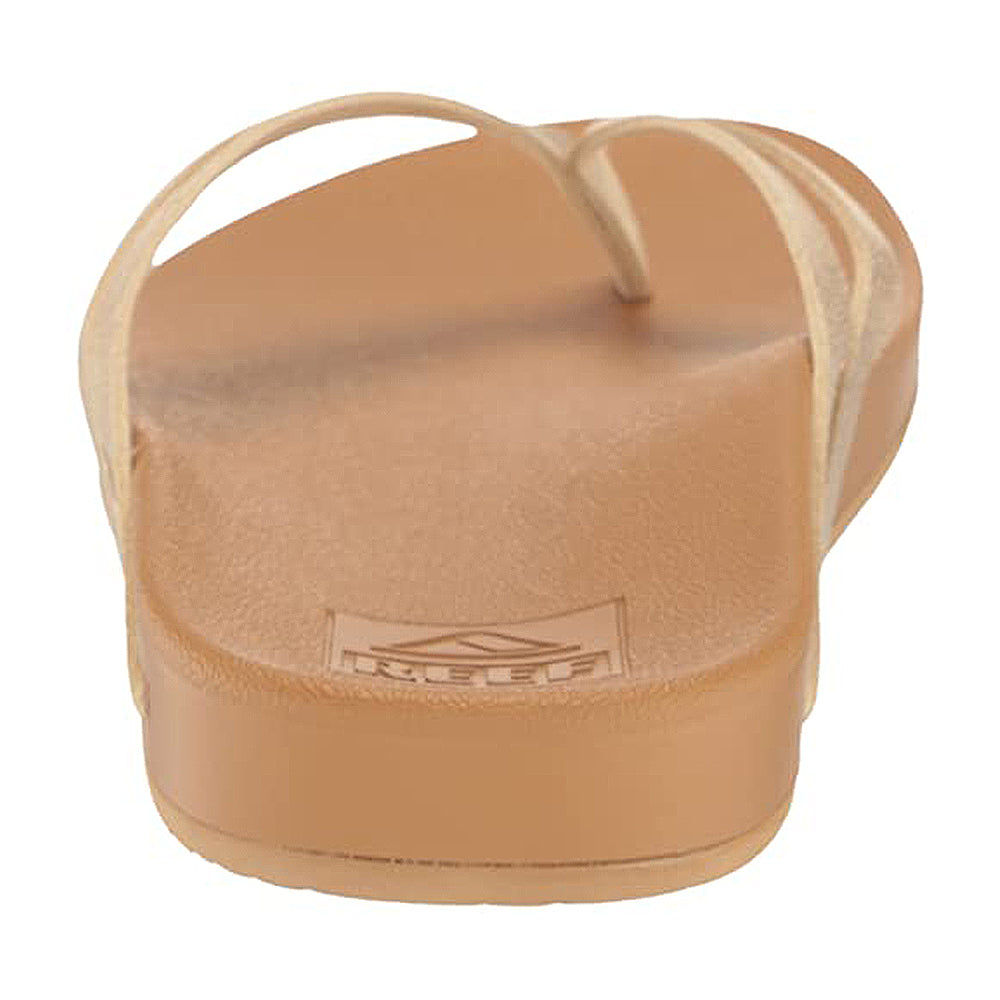 The Reef Cushion Spring Joy womens sandal in tan is shown from the back, featuring a rubber heel, clear straps, and the embossed Reef logo on its cushioned footbed.