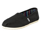 The TOMS Classic Canvas - Men is a black slip-on shoe with a light sole, colorful striped inner lining, and a small TOMS label on the side.