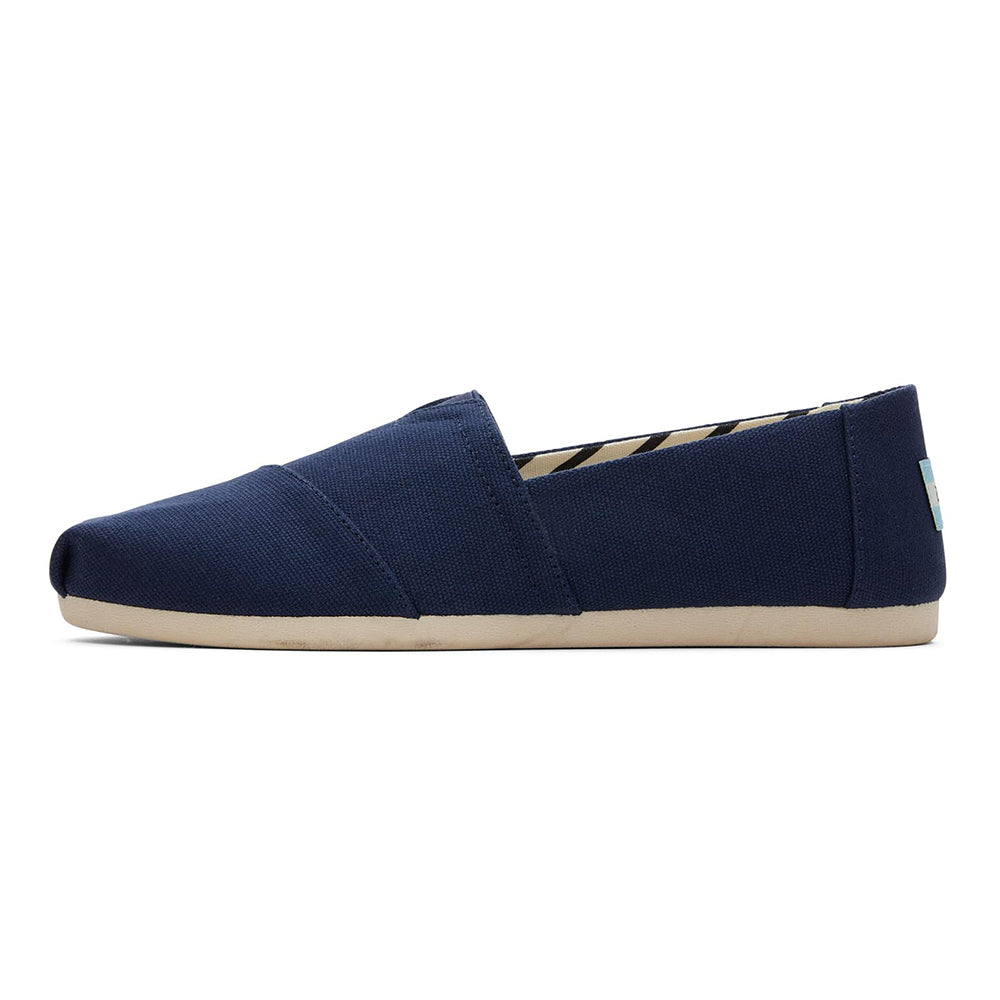The Alpargata ESP - Women by TOMS is a navy blue slip-on canvas shoe with a beige rubber sole and slightly pointed toe—ideal for comfort lovers and fans of the TOMS buy one give one spirit.