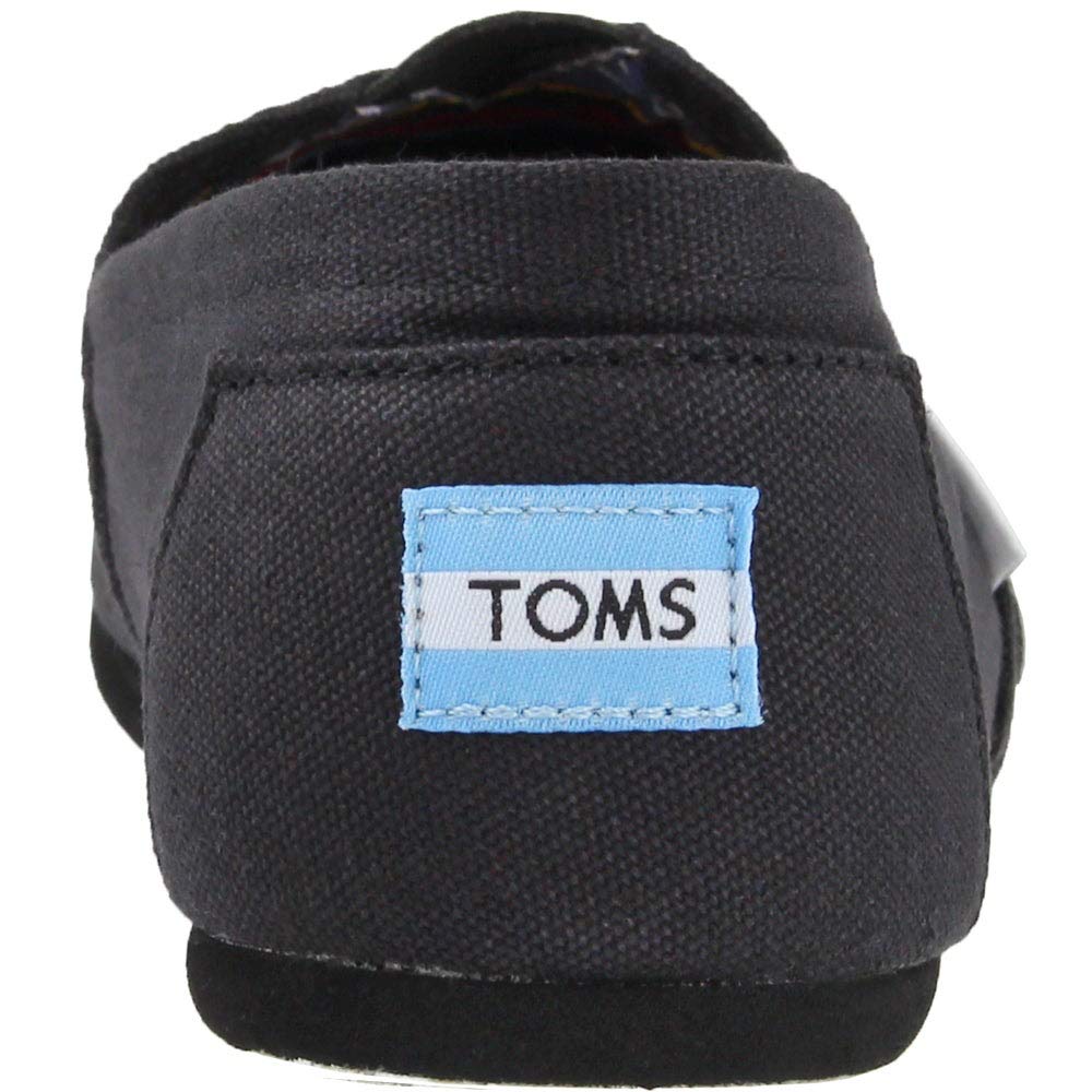 A close-up of the back of a TOMS Classic Canvas - Men alpargata, featuring the light blue and white TOMS logo patch stitched on the black heel.