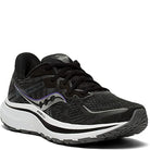 The Saucony Omni 20 Running Shoe - Womens is a black running shoe with white and gray accents, designed for stability and support. It features a thick white sole, black laces, and the Saucony logo on the side, shown from the front and outer angle.