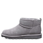 A side view of the BEARPAW Shorty Boots - Womens in gray suede shows a fuzzy lining, flat textured rubber sole, visible stitching, and a pull tab at the back for easy on-and-off.