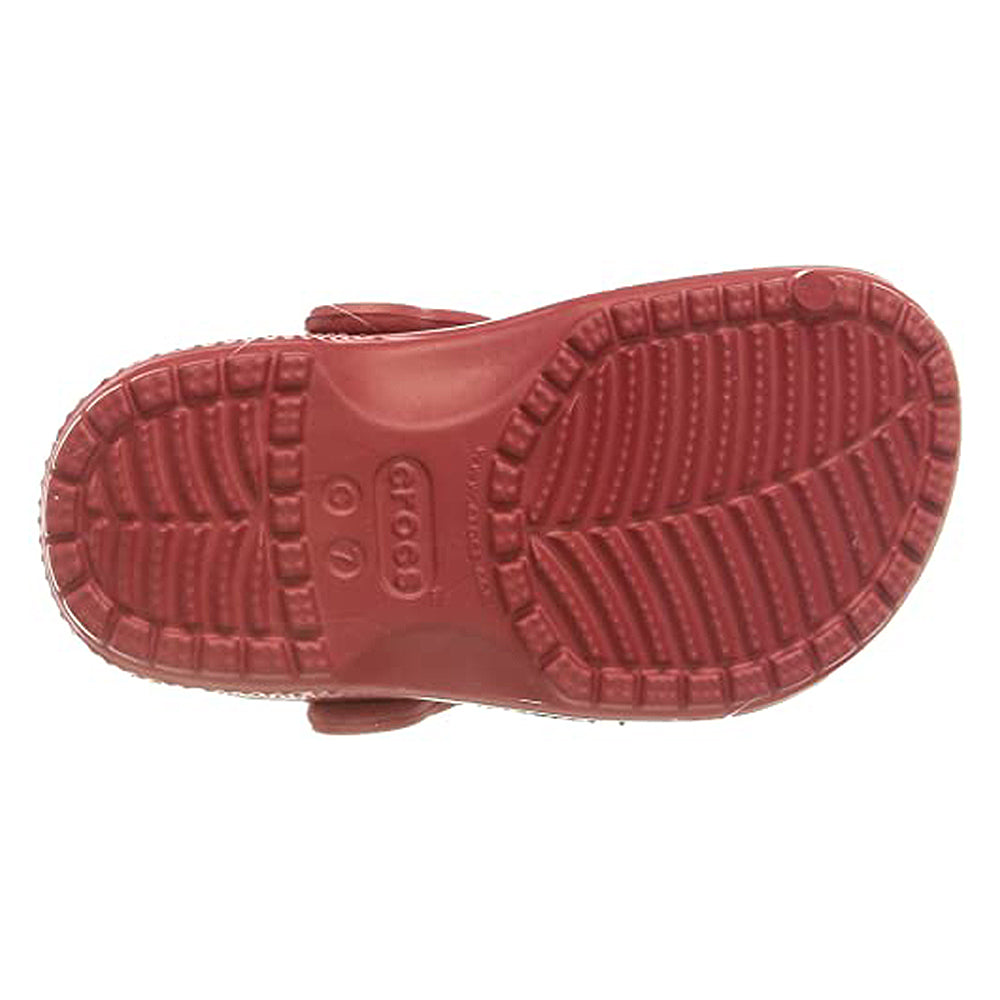 The image displays the sole of a red Crocs Classic Clog for kids, featuring textured treads and grooves for traction. The Crocs logo and size markings are clearly shown in the center.