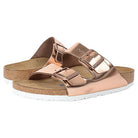 The Birkenstock Arizona - Womens sandals feature rose gold metallic double straps with adjustable buckles, a cork footbed, and white soles for orthopedic walking comfort.