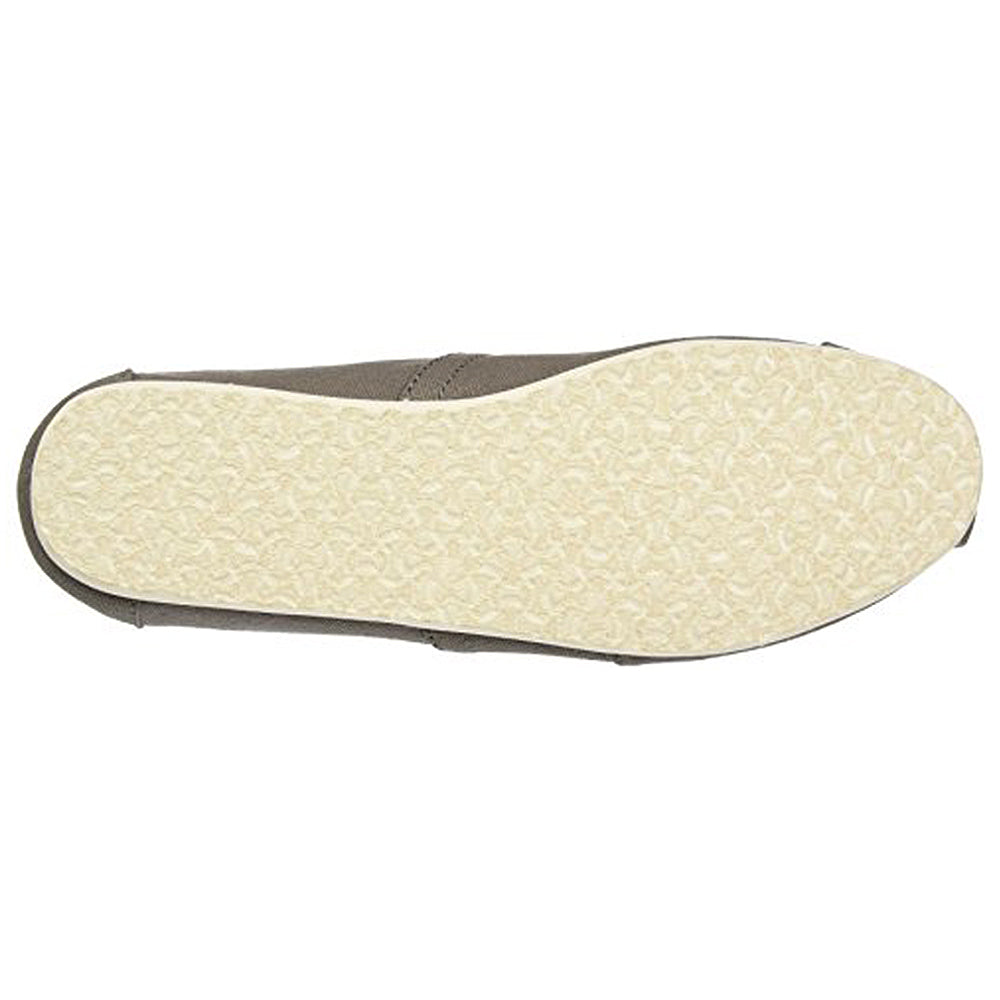 The image shows the bottom view of the TOMS Classic Canvas - Men slip-on, featuring a light-colored, textured rubber sole and a brown upper edge along the sides, resembling an alpargata.