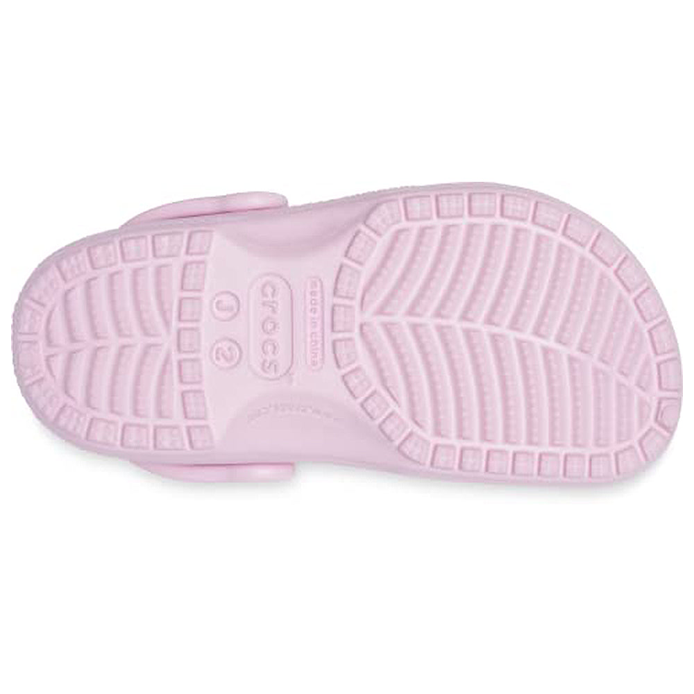 The image shows the sole of a light pink Crocs Classic Clog for kids, featuring a textured tread for grip and the Crocs logo embossed in the center.
