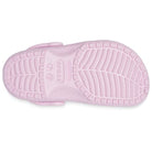 The image shows the sole of a light pink Crocs Classic Clog for kids, featuring a textured tread for grip and the Crocs logo embossed in the center.