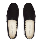A pair of TOMS Classic Canvas - Men black slip-on shoes, viewed from above, with beige insoles featuring the TOMS logo and subtle perforations for breathability.