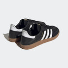 A pair of black adidas Samba Decon Shoes - Men with a leather upper, white stripes, and a brown gum rubber outsole are shown on a light gray background. The heels and insoles are visible, and Samba is printed in gold on the side.