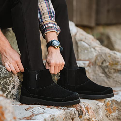 A man wearing BEARPAW Nick Boots and black pants sits on rocks, adjusting a boot. His look is completed with a plaid shirt and a sleek black wristwatch.