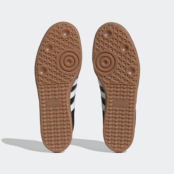 The image features the gum rubber soles of adidas Samba Decon Shoes - Men, highlighting a geometric tread with circular patterns and the adidas logo. The black and white uppers showcase the brands classic, timeless style.