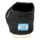 The Classic Canvas - Men slip-on by TOMS is shown from the back in black canvas, with a light blue and white TOMS label on the heel and finished with a white rubber sole.