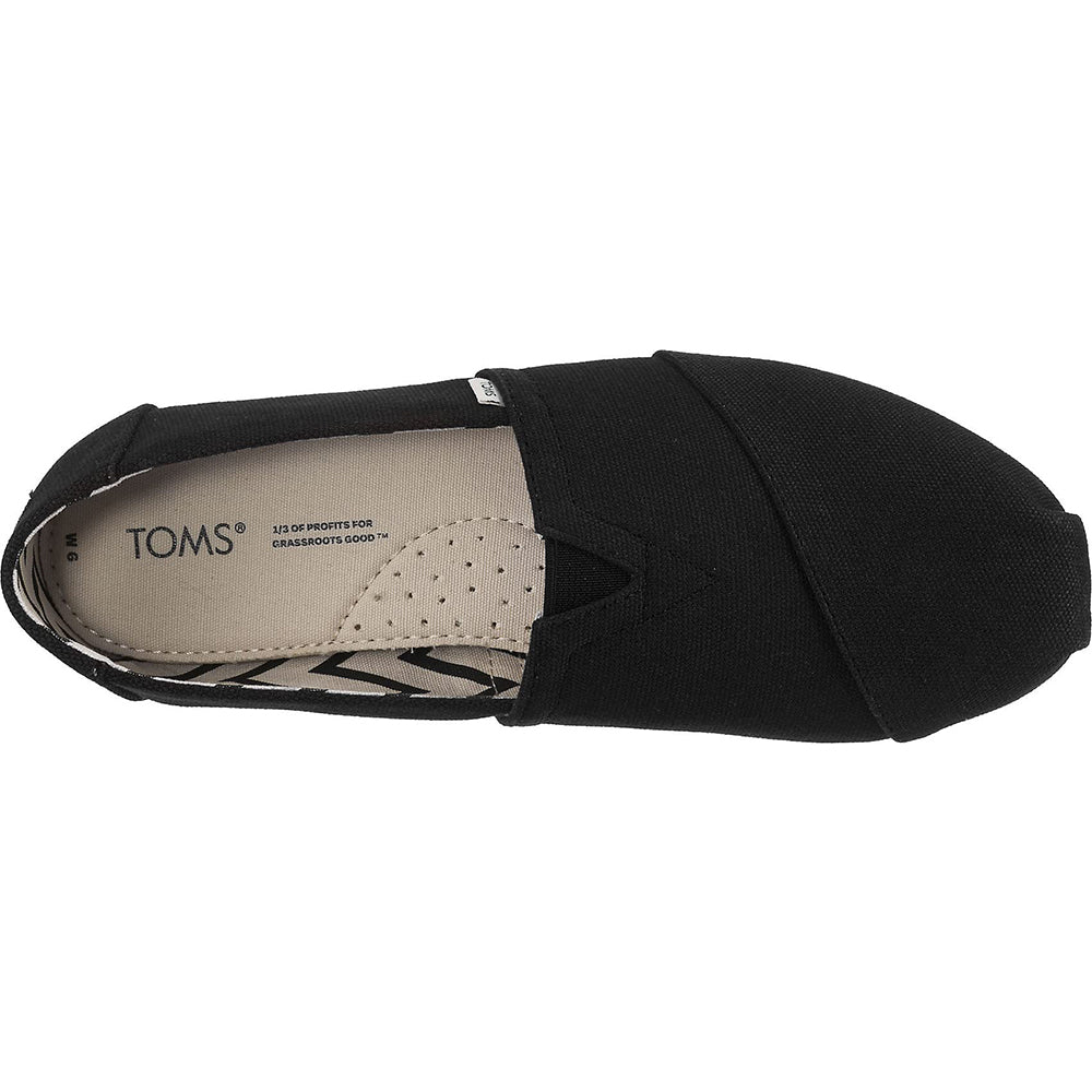Top view of the TOMS Alpargata - Womens slip-on in black canvas, with visible stitching and beige insole showing logo and text about supporting grassroots goods. Made with recycled cotton.