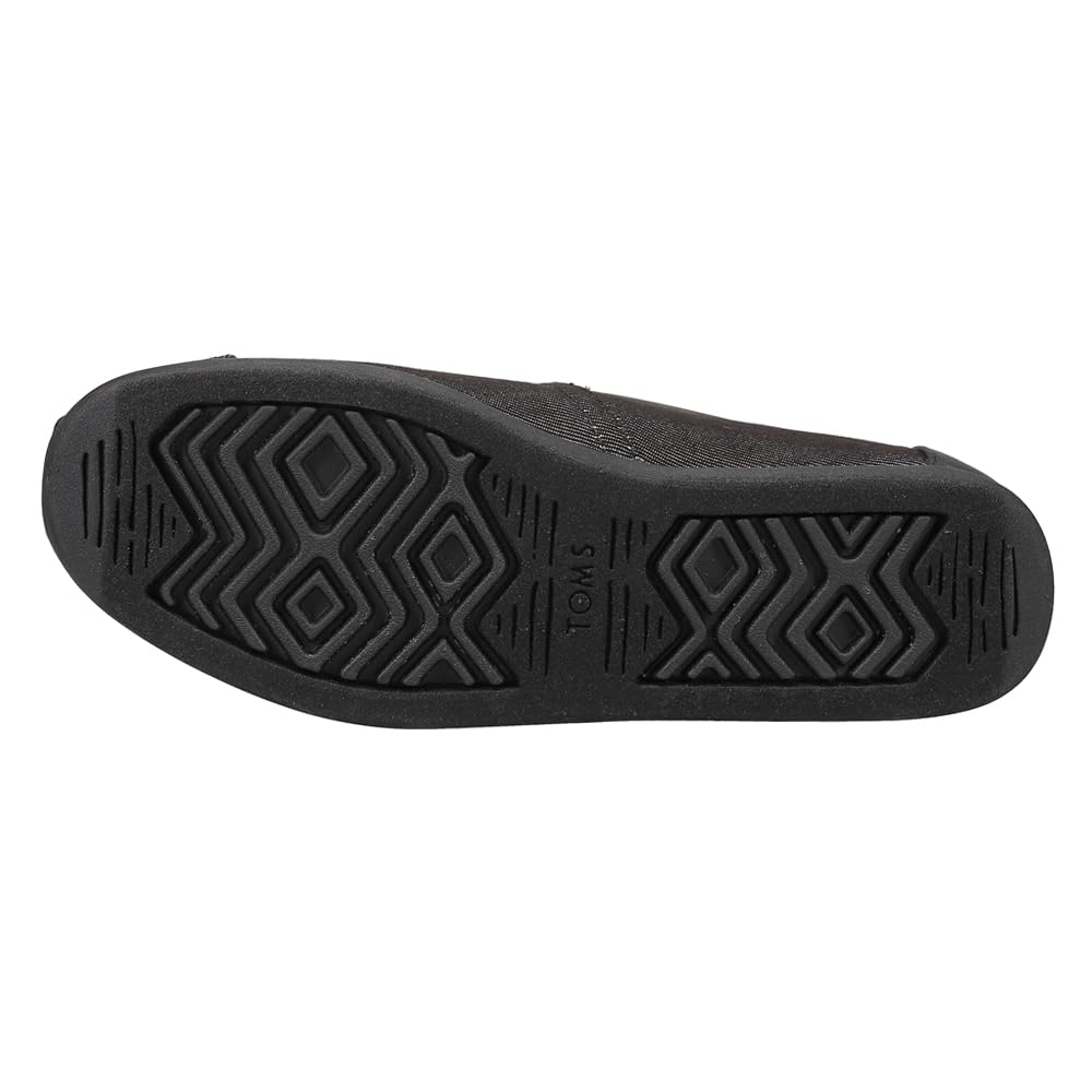 The image displays the black rubber sole of a TOMS Classic Canvas - Men shoe, featuring geometric tread patterns and the TOMS logo imprinted near the center.