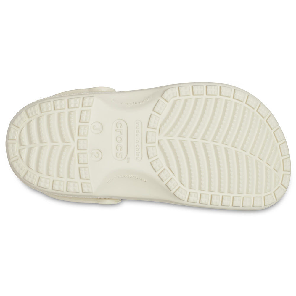 The image shows the sole of a Crocs Classic Clog - Kids in light beige, featuring a textured tread for grip and the Crocs logo with size markings at the center.