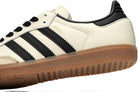 A close-up of the adidas Samba OG - Women sneaker, featuring a leather upper, black stripes with gold SAMBA lettering, a black heel detail, and a light brown gum sole.