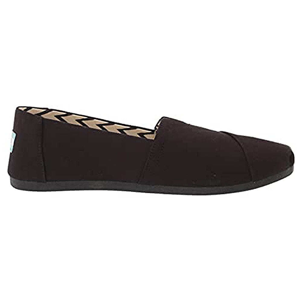 The TOMS Alpargata - Womens slip-on in black features recycled cotton canvas from their earthwise collection, a flat sole, closed toe, and a simple side profile. The inner lining showcases a black and white chevron pattern.