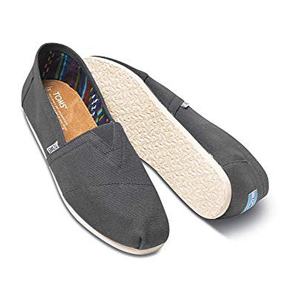 The TOMS Classic Canvas - Men features a black alpargata slip-on design with white rubber soles, a diagonal top seam, colorful striped inner lining, and a small side fabric label.