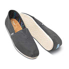The TOMS Classic Canvas - Men features a black alpargata slip-on design with white rubber soles, a diagonal top seam, colorful striped inner lining, and a small side fabric label.