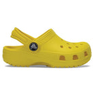 A side view of the Crocs Classic Clog - Kids in bright yellow, featuring ventilation holes and a pivoting heel strap, shown on a white background.
