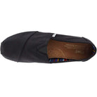 Top view of the TOMS Classic Canvas - Men slip-on in black, with a brown insole and colorful striped heel lining, featuring TOMS branding on the insole and outer tag.