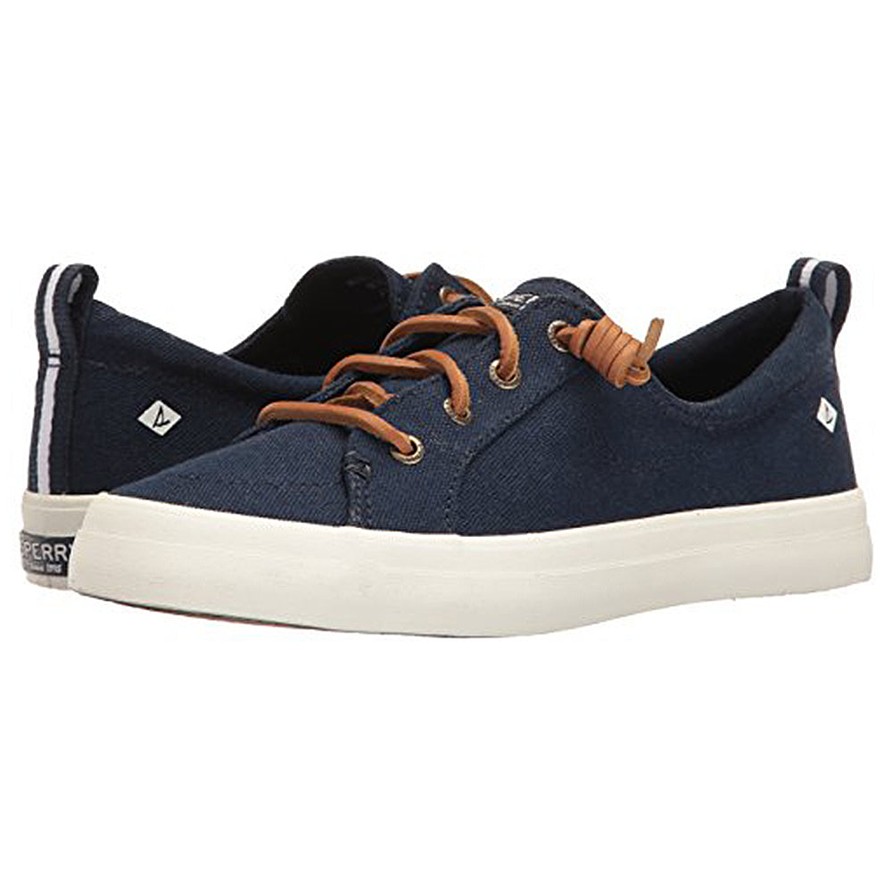 The Crest Vibe - Womens by Sperry is a navy blue canvas sneaker with white rubber soles, brown leather laces, and branding on the heel and side. It’s durable and provides comfortable arch support for all-day wear.